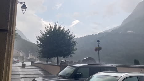 Landscape-shot-rain-and-hail-hitting-cars-during-the-day-in-the-street-of-gavarnie-gedre-village-in-the-wild-pyrenees-mountain-national-parc-with-a-slow-motion