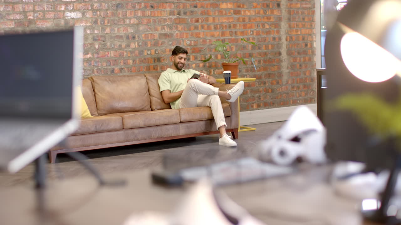 Sitting on couch, man using smartphone and drinking coffee in modern office