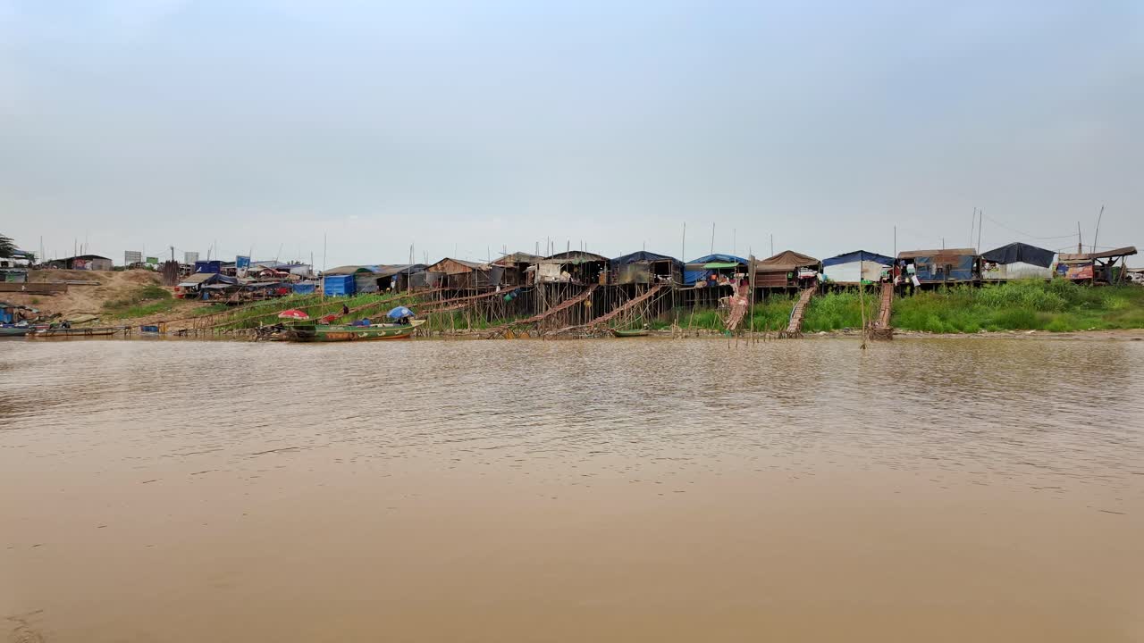 Wide view of traditional stilt houses lined along the edge riverbank of Cambodia.