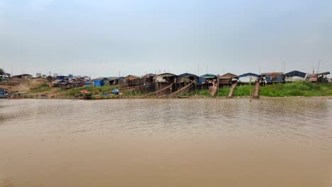 wide view of traditional stilt houses lined along the edge riverbank of cambodia.