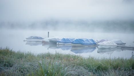 Rechte-Glatte-Dolly-Boote,-Die-Am-Pier-Auf-Einem-Nebligen,-Nebligen-See-Angedockt-Sind,-Berge-Im-Hintergrund