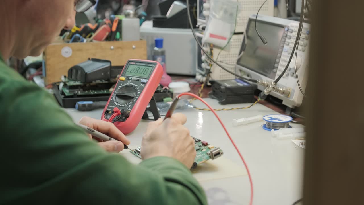 tienda de reparación de equipos electrónicos. el técnico ingeniero soldada la placa de circuitos impresos de un dispositivo electrónico bajo un microscopio.