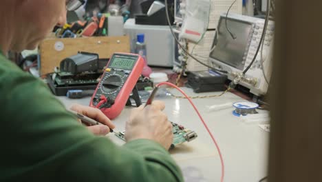 tienda de reparación de equipos electrónicos. el técnico ingeniero soldada la placa de circuitos impresos de un dispositivo electrónico bajo un microscopio.