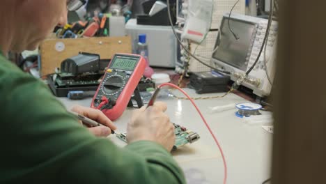 electronic equipment repair shop. the engineer technician solders the printed circuit board of an electronic device under a microscope.