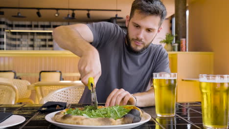 Vorderansicht-Eines-Jungen-Mannes,-Der-Pizza-An-Einem-Restauranttisch-Schneidet