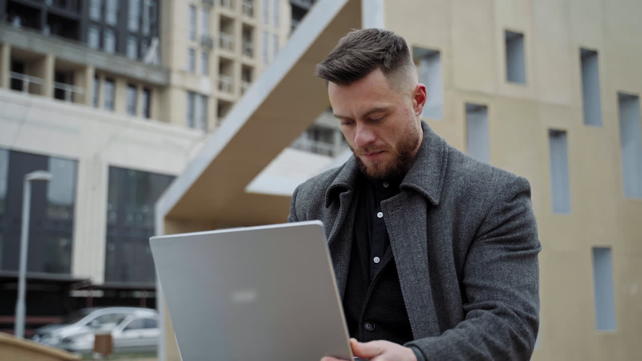 Male using notebook outdoors. Young handsome freelancer sitting with new modern laptop at street