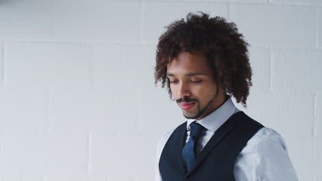 portrait of smiling young businessman wearing suit standing against white studio wall