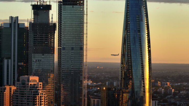 Avião se Aproximando do Aeroporto de Sydney por Trás dos Arranha-Céus Ultramodernos na Cidade ao Pôr do Sol