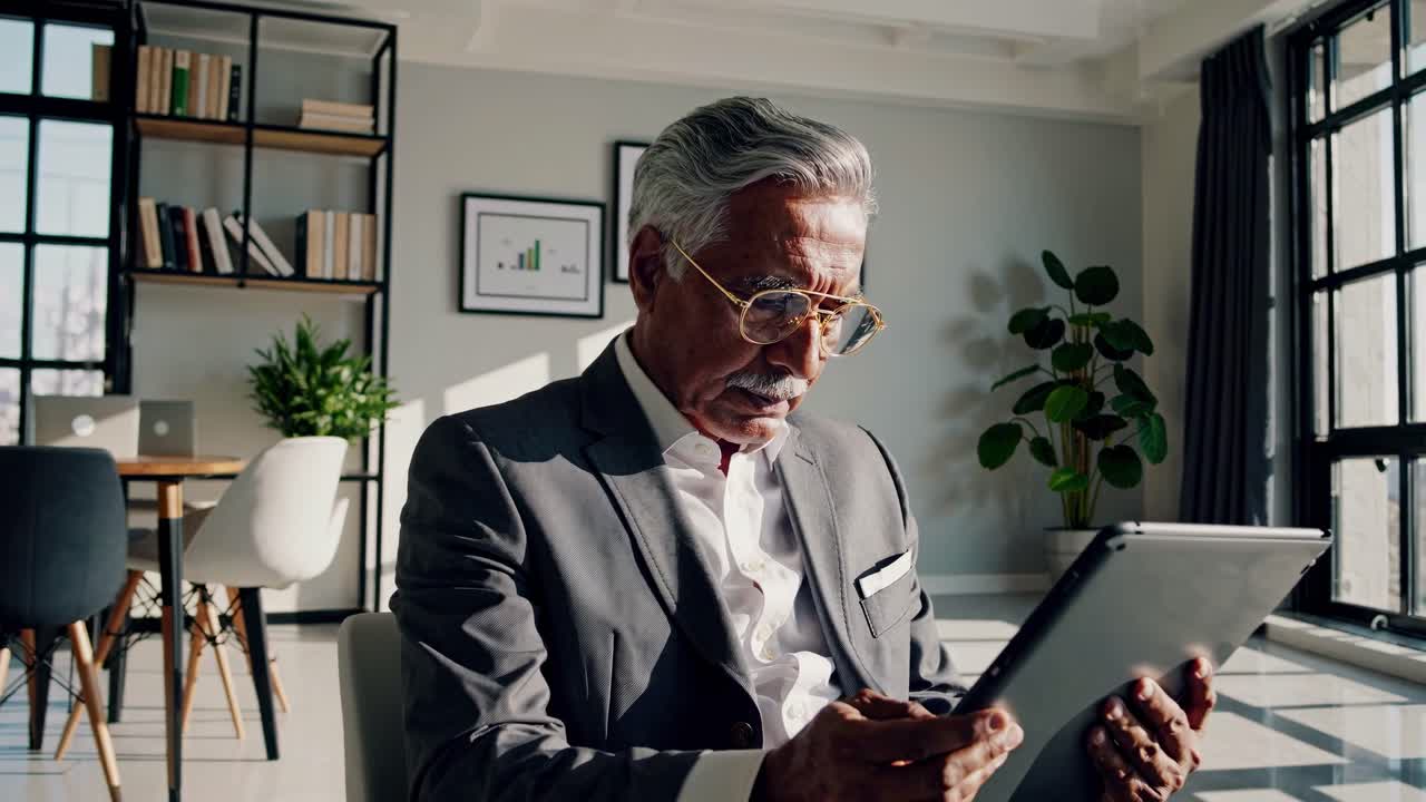 En moden mann i dress leser et nettbrett på et moderne kontor. Videoen bruker et lavt vinkel-bilde.