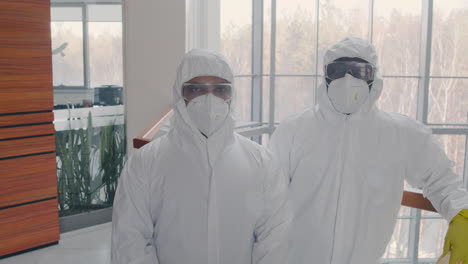 two cleaning men wearing personal protective equipment looking at camera inside an office building