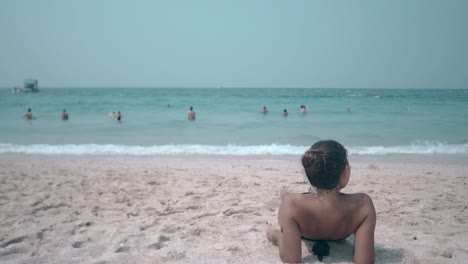 brunette-rests-on-sandy-beach-on-sunny-summer-day-backside