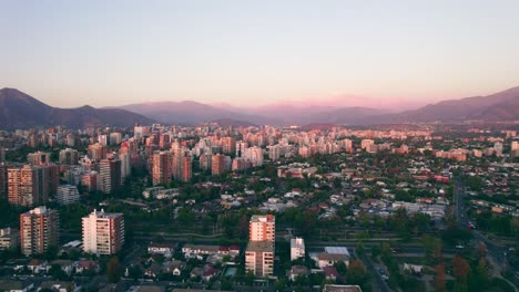 órbita aérea de las condes, un barrio rico y tranquilo de la ciudad, cordillera de los andes iluminada al fondo, puesta de sol épica