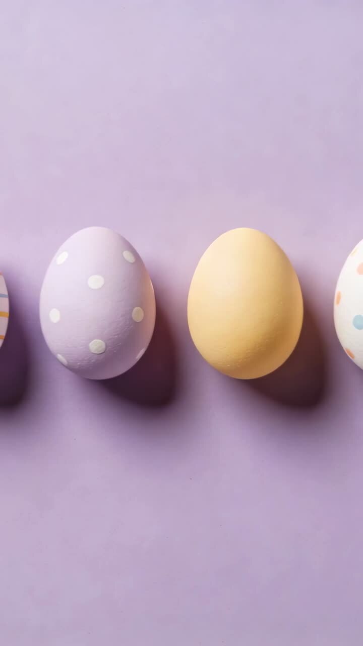 Panning camera revealing decorated pastel eggs on purple tabletop, showing soft shadows beneath