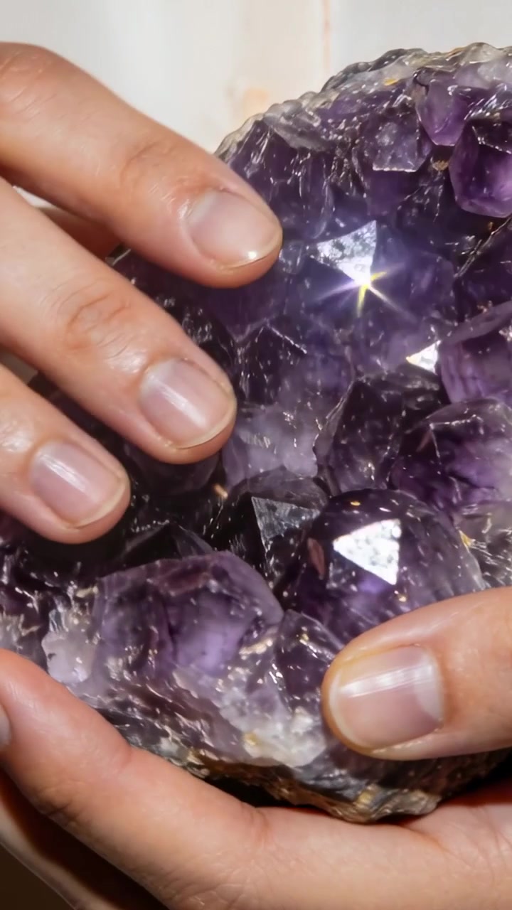 Vídeo vertical: Mãos adultas segurando geodo de ametista roxa para exame de perto em sala