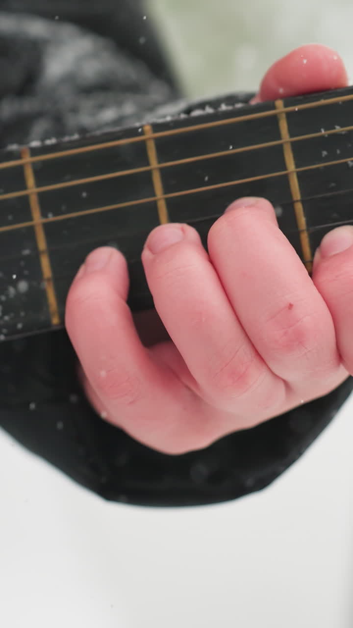 mano tocando la guitarra en cuerdas de polvo de nieve, mostrando la armonía de la música y la belleza del invierno, texturas heladas en la manga negra y el cuello de la guitarra