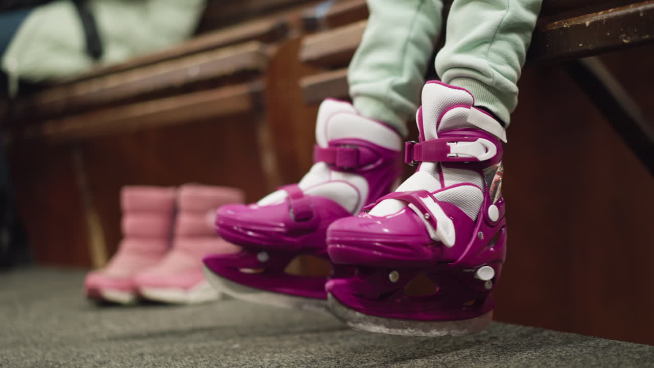 Close-up of a child's legs in pink and white ice skates with pink shoe close by, playfully dangling and moving above the ground