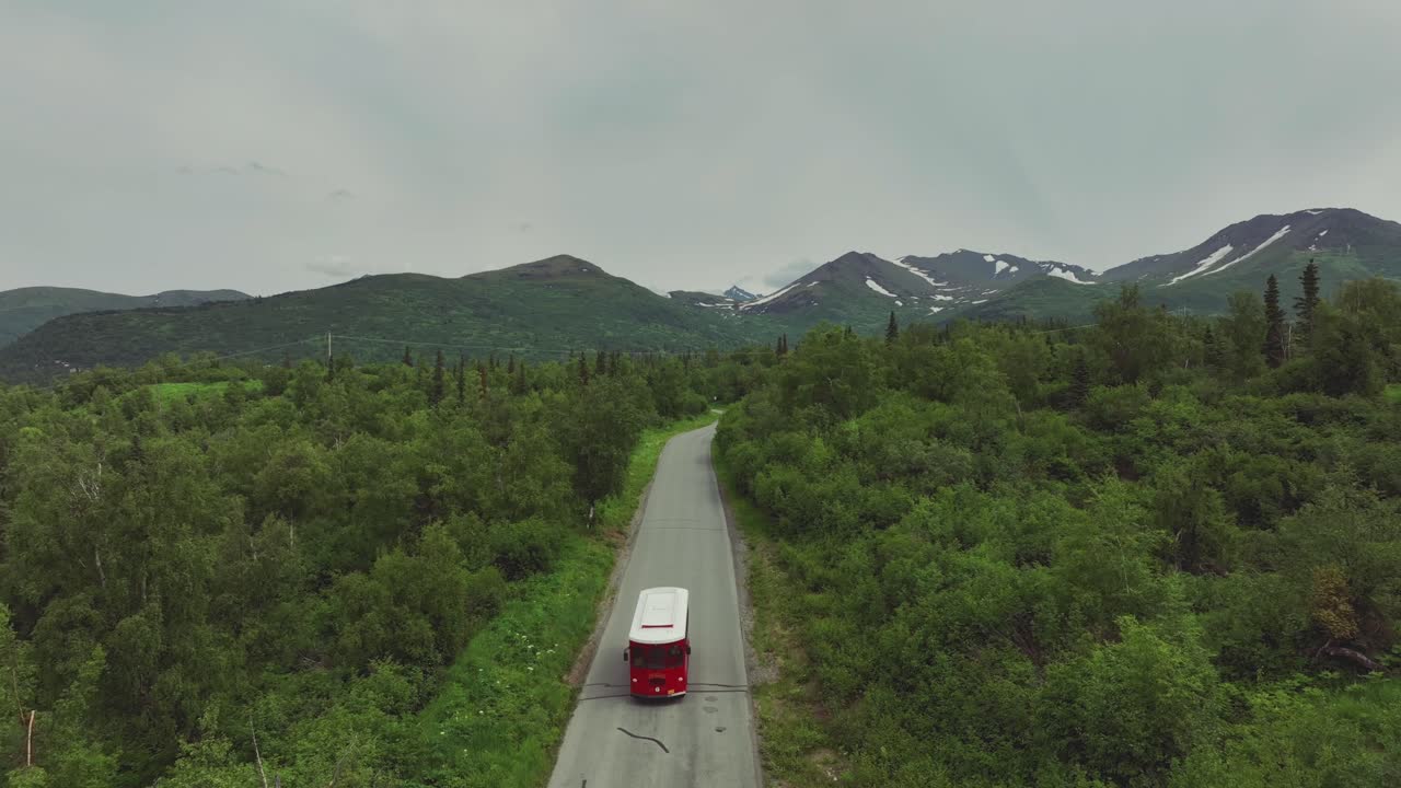 Veduta aerea di un autobus turistico rosso che viaggia nella suggestiva campagna di Anchorage in Alaska - ripresa all'indietro del drone