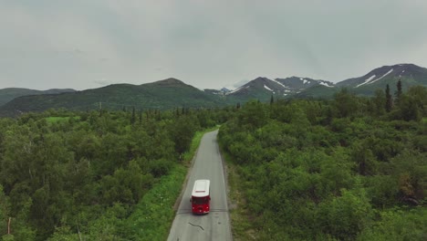 Aerial-View-Of-Red-Trolley-Bus-Traveling-In-Scenic-Countryside-Of-Anchorage-In-Alaska---drone-pullback