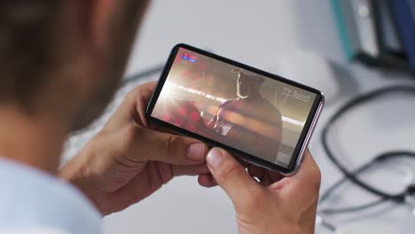 compuesto de un médico masculino viendo un evento deportivo en un teléfono inteligente