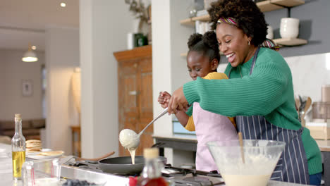 Happy-african-american-mother-and-daughter-frying-pancakes-in-kitchen,-slow-motion