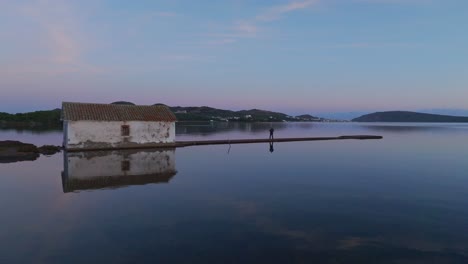 Water-reflected-landscape-with-a-lonely-abandoned-white-house-aerial-revealing-establishing-shot