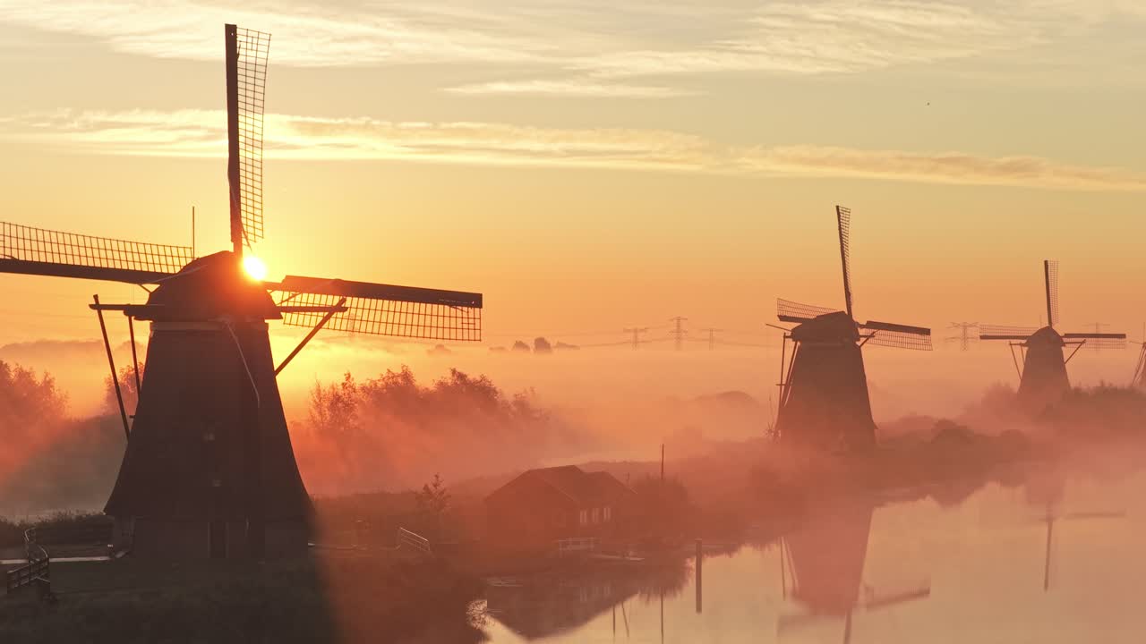 Hollanda'da sisli Kinderdijk kanalları ve yel değirmenleri üzerinde panoramik gün doğumu