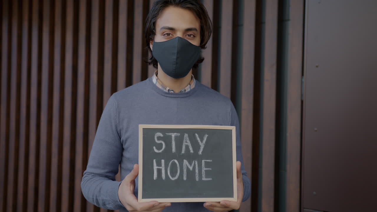 Man holding a sign that says 'Stay Home' during a pandemic.