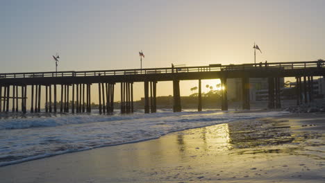 dolly shot moving backwards along the ventura beach with the pier withsunset in the background located in southern california