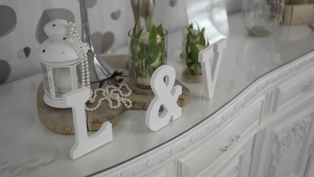 White wedding decor featuring initials, a pearl-draped lantern, and greenery in a chic setting