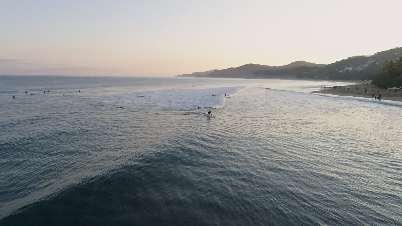 Aerial of silhouetted surfer as they ride wave in during beautiful sunrise, 4K