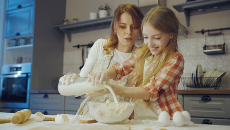 une adolescente mignonne cuisine un daugh et y verse du lait pendant que sa mère l'aide dans la cuisine. à l'intérieur