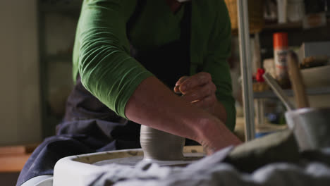 mid section of male potter creating pottery on potters wheel at pottery studio