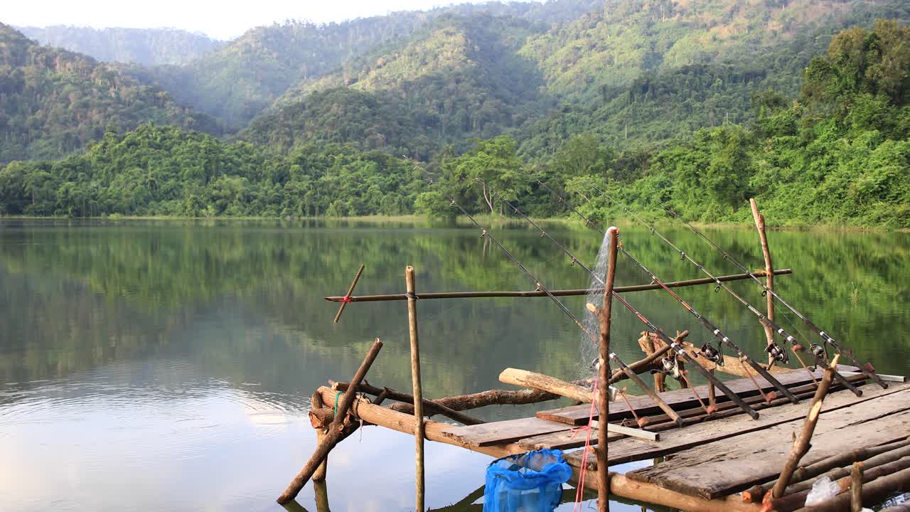 un grupo de cañas de pescar al final de un muelle esperando pescar en el lago con fondo forestal