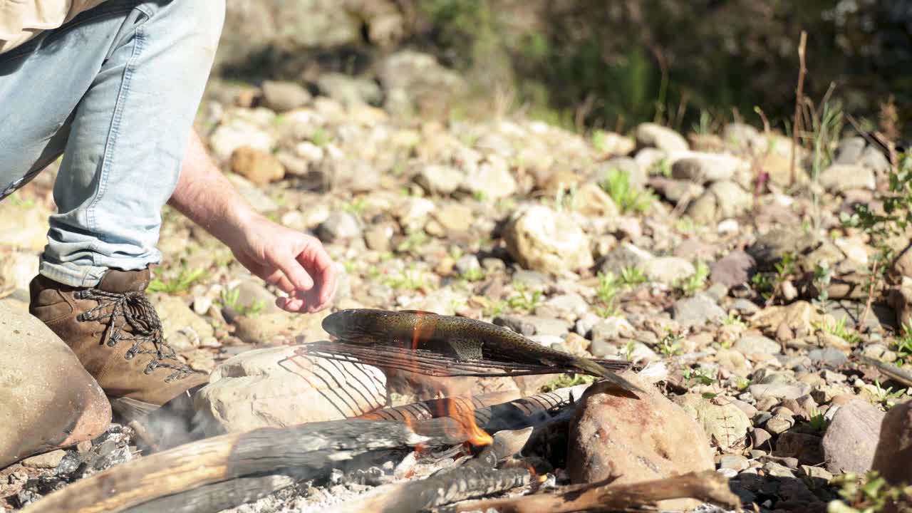 Close up shot of a bushman cooking a brown trout over a fire in the Victorian high country