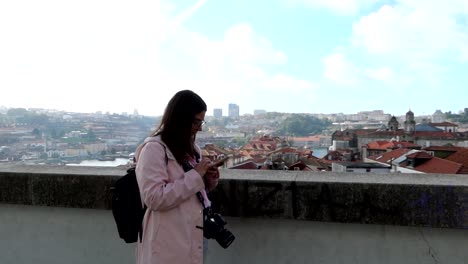 woman typing on her phone in front of porto cityscape on cloudy day