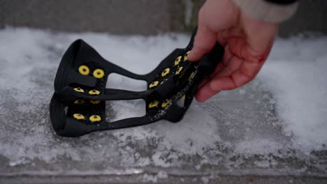 person places pair of micro spikes for shoes on icy sidewalk