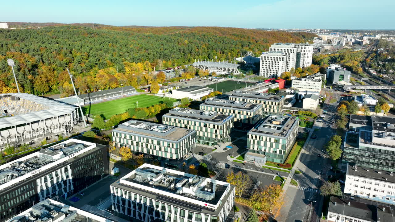 Aerial view of modern office buildings and football stadium in Gdynia surrounded by autumn forest and city skyline