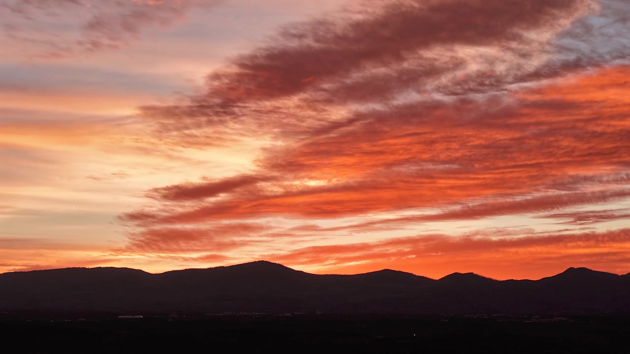 4K drone timelapse captures dramatic fire orange sunset clouds shifting over a southwestern mountain peak. Cinematic atmospheric transition featuring warm sky colors and wilderness scenery.