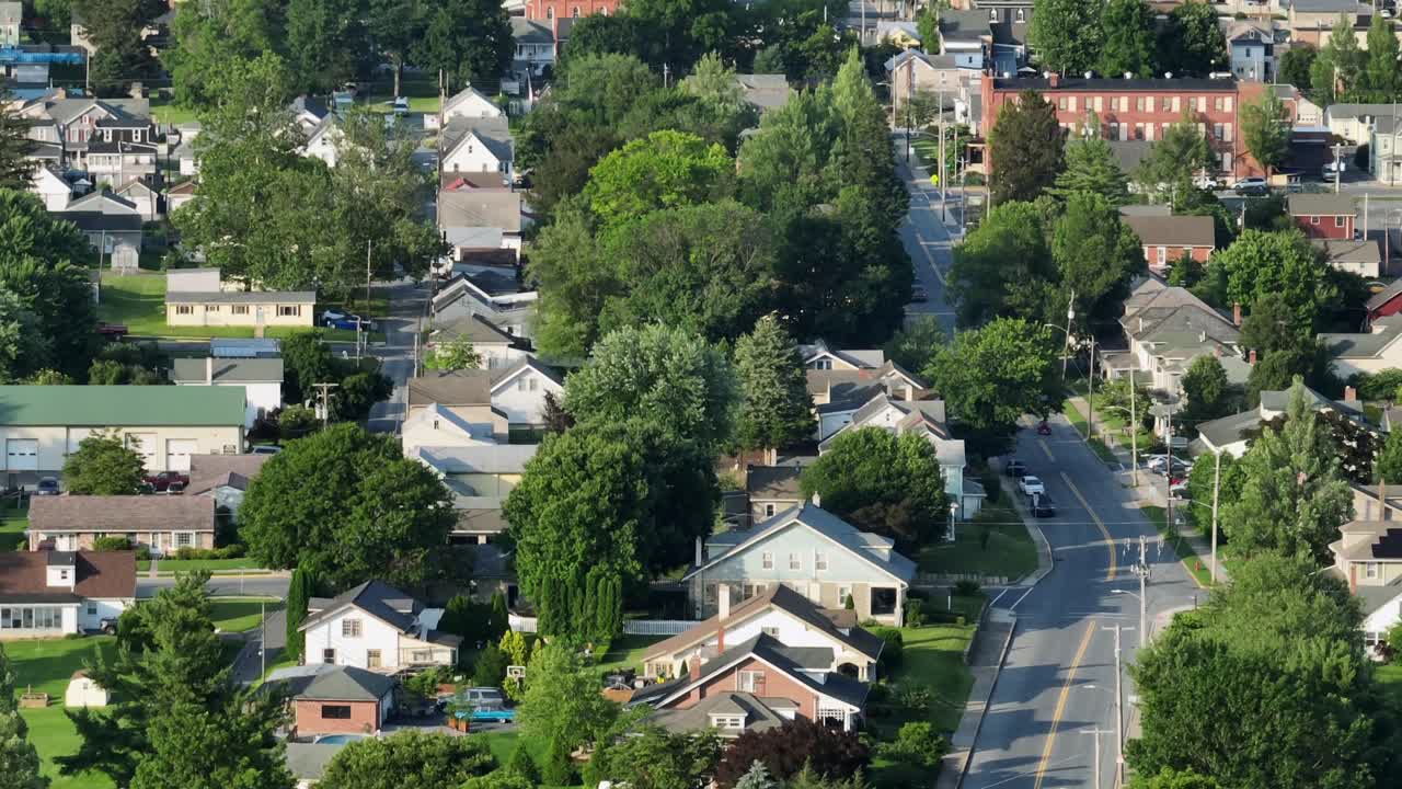 American city neighborhood with houses along tree-lined road in summer. Aerial zoom wide shot. Historic buildings with different architectural style and colors. Sunset evening in USA
