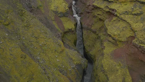 Un-Desfiladero-De-Rocas-En-Capas-Con-Agua-Que-Corre-Por-Un-Valle-Angosto-Entre-Una-Montaña,-Con-Paredes-Rocosas-Escarpadas-Y-Un-Arroyo-Que-Lo-Atraviesa-Formando-Una-Cascada