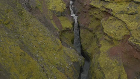 un desfiladero de rocas en capas con agua que corre por un valle angosto entre una montaña, con paredes rocosas escarpadas y un arroyo que lo atraviesa formando una cascada
