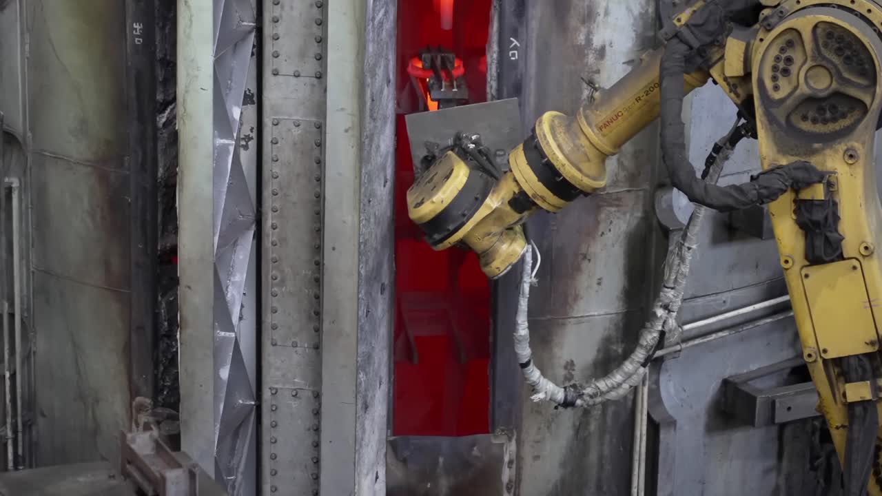 Braccio robotico industriale che solleva un anello di metallo incandescente da una fornace e lo colloca in una camera di raffreddamento o tempra