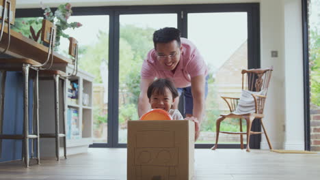 asian father and son pushing son around kitchen floor at home in junk modelled car