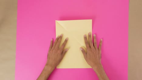 folding corners of decorative paper on pink paper for origami