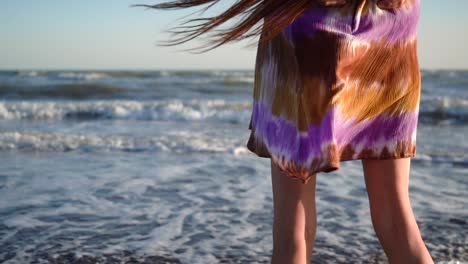 woman in dress standing in the beach with waves meeting the sandy shoreline. - static, crop