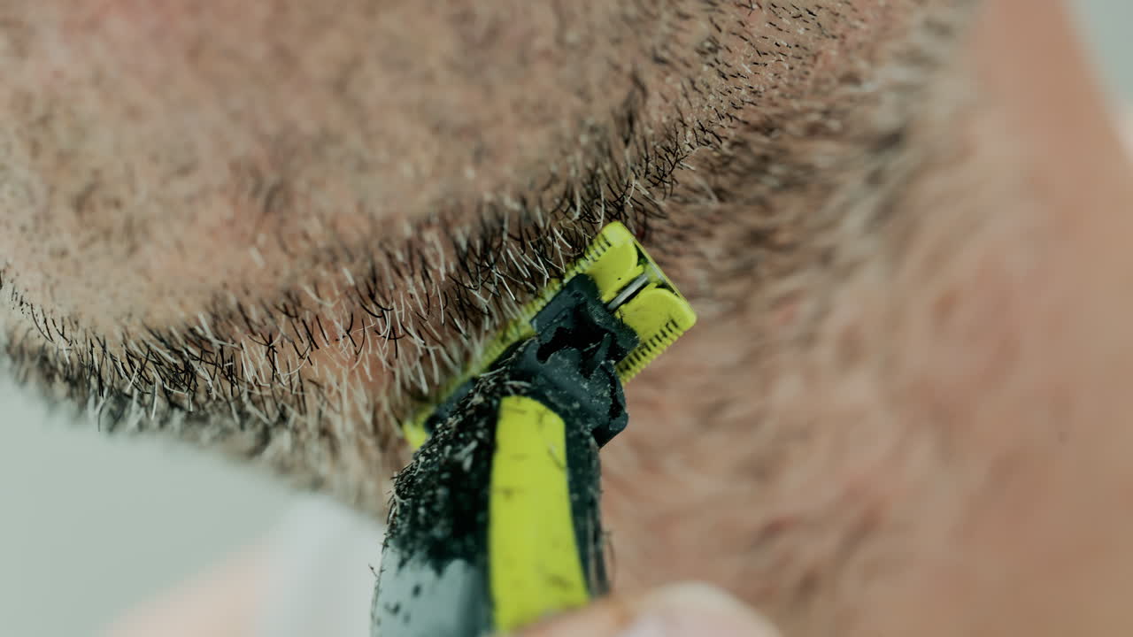Close up of a man using an electric razor to trim facial hair in the bathroom