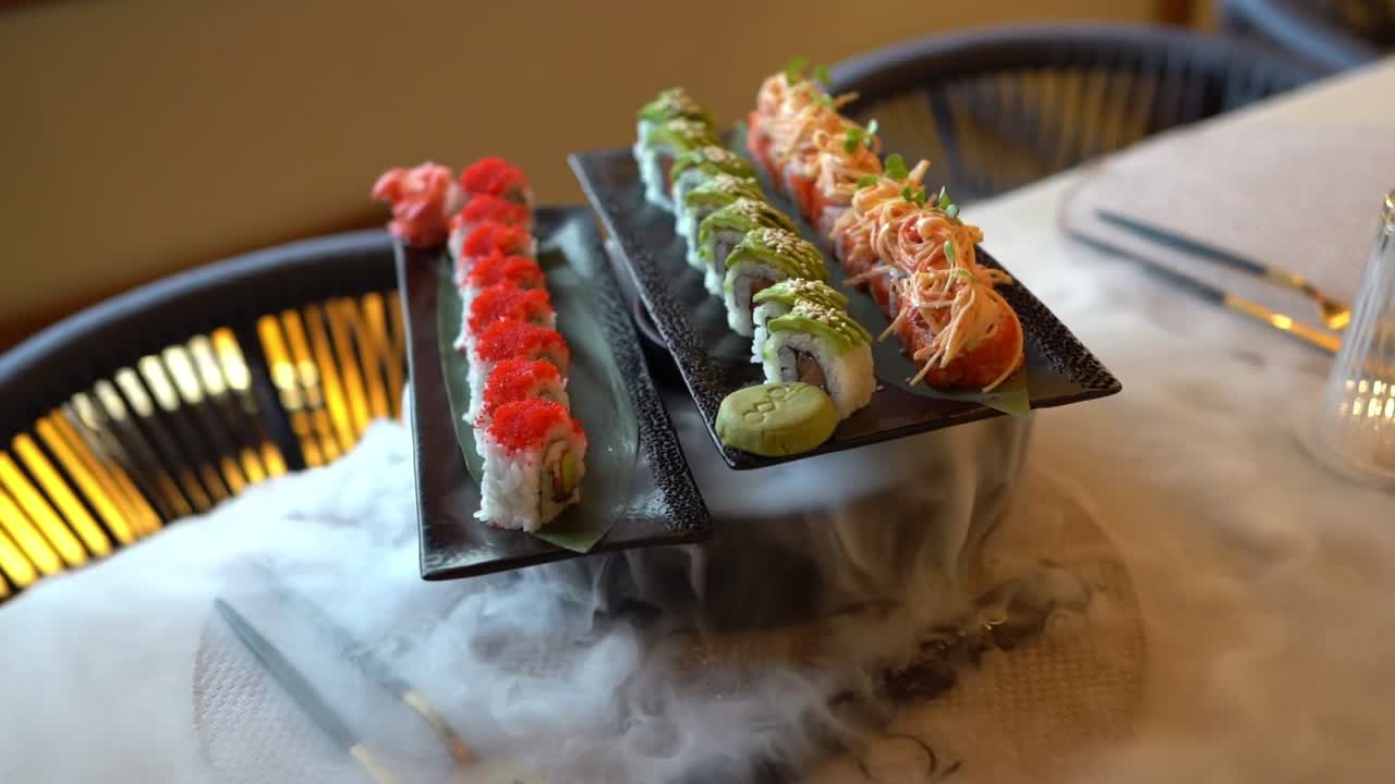 Colorful sushi rolls served on black trays with a smoky presentation, close up shot