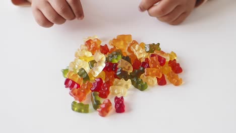 a child's hand reaches out to a pile of colorful gummy bears