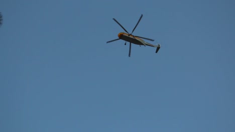 un helicóptero de extinción de incendios vuela directamente sobre nosotros buscando agua para un incendio forestal cercano y desaparece detrás de los árboles.