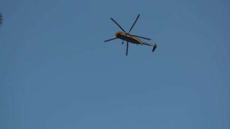 a firefighting helicopter flies directly overhead searching for water for nearby forest fire wildfire and disappears behind trees